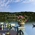 Scenic Lakeside View with Gondola Hillside Trees Blue Sky and Flower Vases on Terrace Table