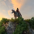Ancient Warrior on Horseback Standing Atop Hilltop With Green Trees and Sunset Sky