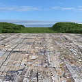 Construction Site Featuring Weathered Concrete Slabs Cracks Green Vegetation Low Hills Under Blue Sky