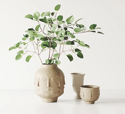 Face Shaped Ceramic Vase With Lush Green Leaves And Small Accompanying Vessels On White Surface 3d model