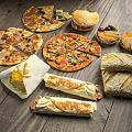Assorted Delicious Food Including Pizzas Burgers Wraps And Fresh Bread On Wooden Table