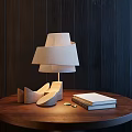 Modern Layered Linen Shade Table Lamp On Round Wooden Table With Books And Dark Wall