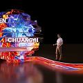 Illuminated Spherical Structure With WEICHEN CHUANGYI Text And Person Standing Beside Glowing Streamline Decoration