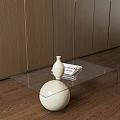 Glass Coffee Table With White Spherical Base And White Vase Stacked Books On Wooden Wall Floor