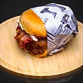 Juicy Hamburger Wrapped in Newspaper on Wooden Round Tray with Bacon Patty and Sauce