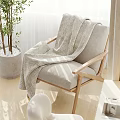 Light Gray Leisure Chair With Wooden Armrests And Textured Blanket Near Potted Plant