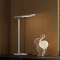 White Illuminated Table Lamp On Wooden Table With Rabbit Shaped Decor And Blinds