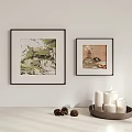 Framed Artworks On White Wall With Tabletop Candles And Decorative Pinecones
