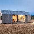 Modern Guesthouse Building In Field With Illuminated Interior And Outdoor Seating