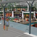 Vibrant Commercial Street Featuring Glass Canopy Lush Greenery Escalators Red Seating And Busy Shoppers