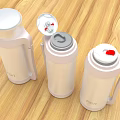 Three White Thermal Mugs With Different Lid Designs Handles On Wooden Tabletop