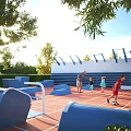 Outdoor Playground Area With Adults And Children Playing On Red Flooring Blue Structures And Trees