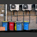 Different Colored Trash Bins And Wall Mounted Fans Near Brick Wall On Ground With Rubbish