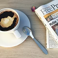 A Cup of Coffee with Latte Art on Saucer and Spoon Next to Newspaper
