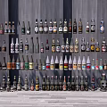 Neatly Arranged Wine Bottles and Glasses Against Gray Wall on Gray Floor With Various Colors Shapes