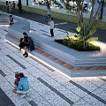 Modern Outdoor Public Bench In Urban Plaza With Green Plants Pedestrians And Stone Pavement