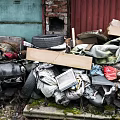 Waste Pile with Tire Wooden Board Fabric Old Electronics Cardboard Boxes and Red Brick Wall
