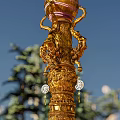 Golden Columnar Landscape Sculpture Surrounded by Pine Trees Blue Sky and Stone Steps