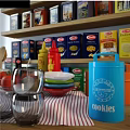Kitchen Utensils Display With Wooden Spoons Tomatoes Glass Cups And Boxed Food On Shelves