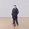 Woman Wearing Black Coat And Dark Pants Walking On Wooden Floor With Light Background
