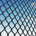 Black Diamond Mesh Fence With Metal Links Against Blue Sky And White Clouds