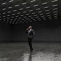 Businessman In Suit Talking On Phone In Large Empty Room With Ceiling Lights