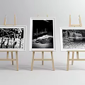 Art Supplies Display Featuring Three Wooden Easels With Black And White Landscape Paintings In Frames