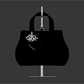 Black Quilted Handbag With Handles And Small Decorative Charm On Transparent Display Stand