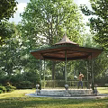 Garden Landscape With Tall Trees Person Leaning Against Tree Bicycle And Sunlit Pavilion Path