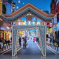 Tibetan Style Commercial Street With Traditional Archway Night Lights Pedestrians And Colorful Shop Signboards