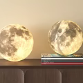 Glowing Moon Shaped Decorative Lamps On Wooden Shelf With Stacked Books