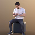 Man in white T-shirt and ripped jeans sitting on gray cylindrical object using smartphone