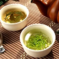 Traditional Tea Set With White Teacups Green Tea Leaves And Brown Teapot On Bamboo Mat