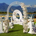 Scenic Garden Landscape With White Floral Archway Circular Ornament Pillars Lawn Lake And Mountain Backdrop