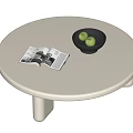 White Round Coffee Table With Open Magazine Black Bowl And Green Fruits