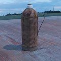 Woven Rattan Thermos Flask Placed On Wooden Floor With Open Field And Sky