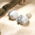 White Wireless Earbuds On Sandy Ground With Wooden Branch And Stones