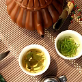 Traditional Tea Set With White Teacups Green Tea Leaves And Brown Teapot On Bamboo Mat