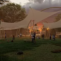 Tensile Membrane Structure In Outdoor Park With Green Grass People Activities And Sunset Sky
