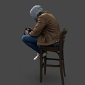 A Man Sitting On Wooden Chair Holding Camera Wearing Brown Jacket Gray Hoodie Blue Jeans