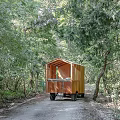 Wooden Trailer Style Cabin Surrounded by Trees with Two People Resting Outside