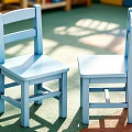 Two Blue Wooden Kids Chairs In Bright Playground With Green Floor