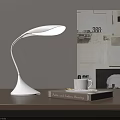 Modern White Desk Lamp With Curved Design On Wooden Table Beside Collage Wall Art