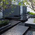 Modern Building Exterior Wall With Stone Cladding Water Feature Landscaped Greenery And Accent Lighting
