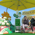 Two People Sitting Under Yellow Umbrella At Shining Yoke Park With Balloons And Sunshine