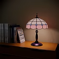 Stained Glass Table Lamp With Pink Blue Shade Black Base On Wooden Shelf With Books
