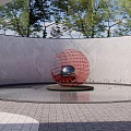 Red Spherical Sculpture With Silver Center In Circular Pool Surrounded By Trees And Gray Wall