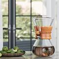Glass Coffee Pot With Wooden Handle And Lime Plate Near Window With Green Plants Background