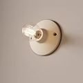 Minimalist White Wall Lamp With Round Base And Transparent Bulb On Light Colored Wall