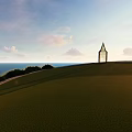 Scenic Green Grassland With Tall Spire Structure Overlooking Sea Under Blue Sky With Clouds